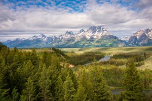 River passing through the green fields of Grant Teton National Park with mountains in the background